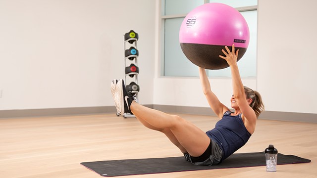 A woman lifting an exercise ball while doing a V-up