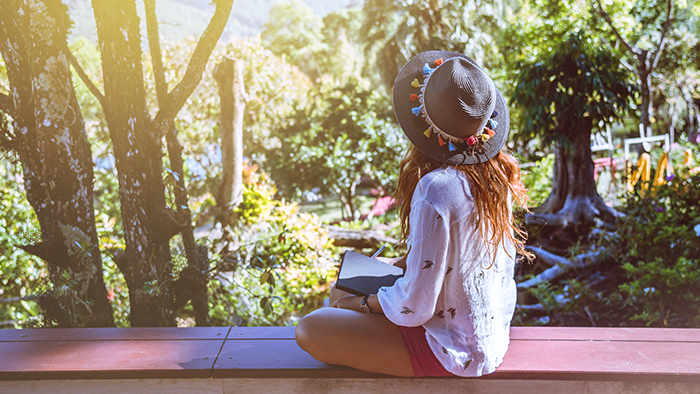 A girl sitting on a ledge looking out at scenery with her journal