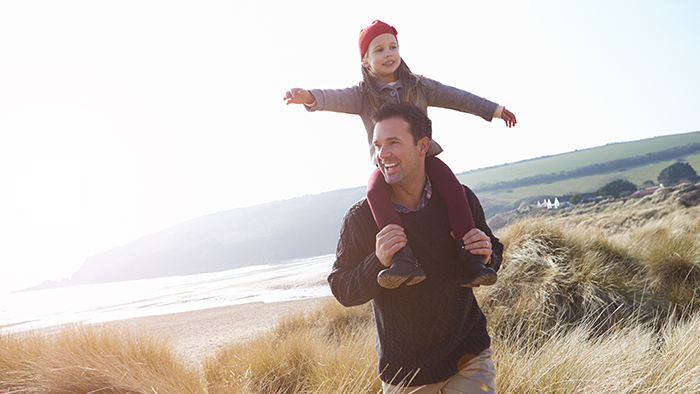 Father holds daughter on his shoulders by the beach