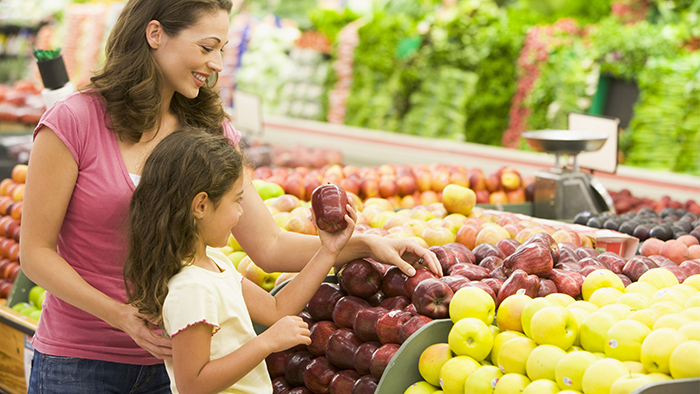 Mother and daughter grocery shopping and looking at apples.