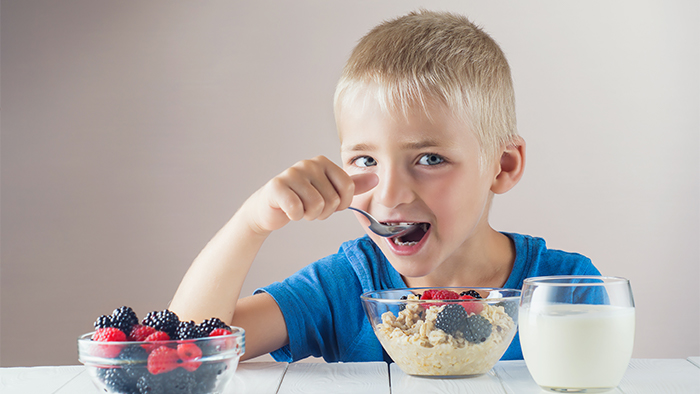 Young boy eating oatmeal, granola, and berries with a glass of milk on the side.