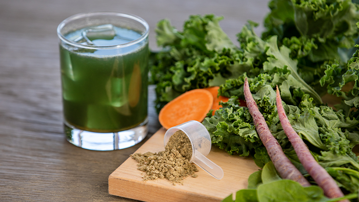 A glass of Organic Greens next to fresh vegetables