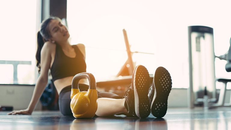 A woman sitting on the gym floor with a kettlebell