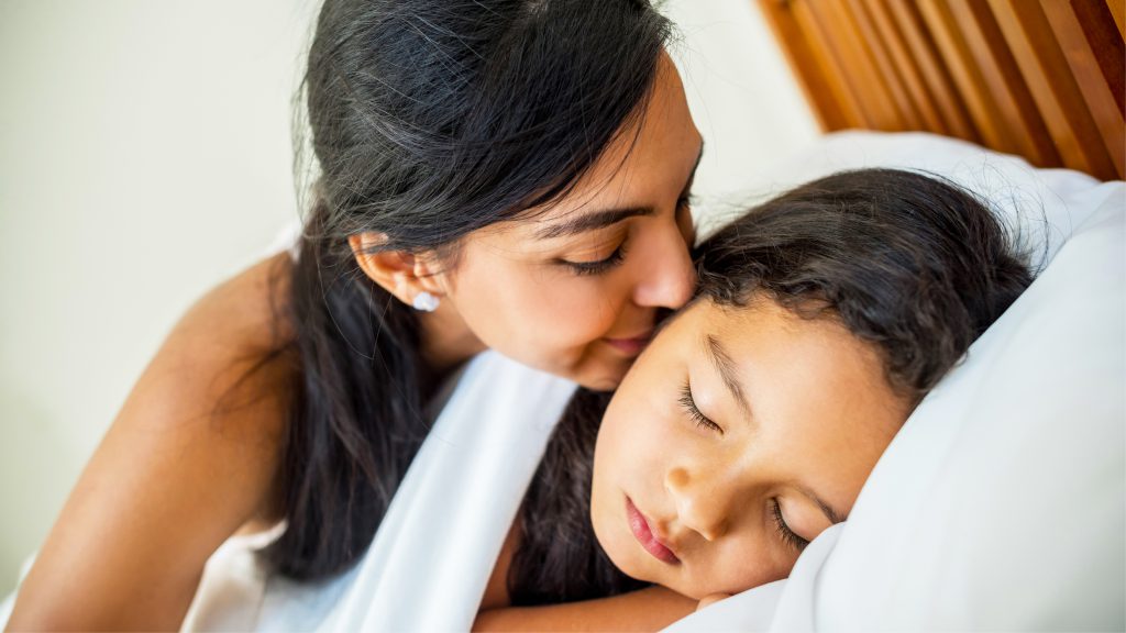 Mom kissing her daughter's cheek in bed