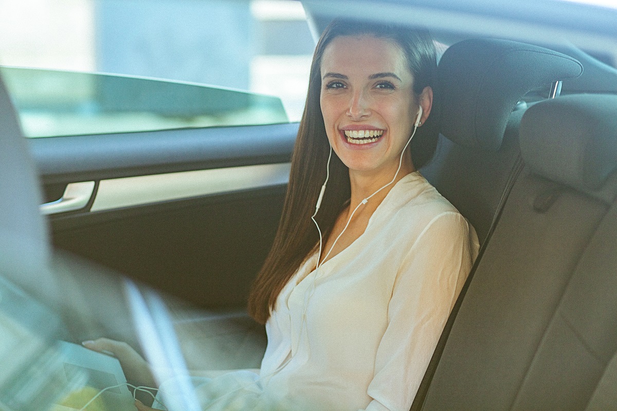 A woman smiling and listening to earbuds in the car