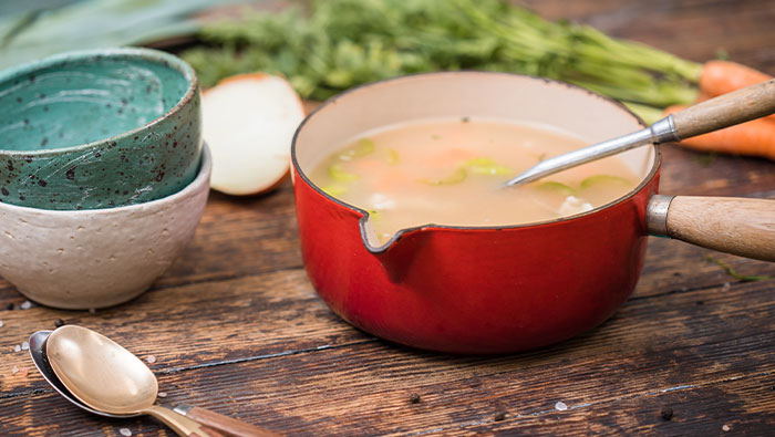 Saucepan with leftover turkey and vegetable soup with bowls and vegetables on the table