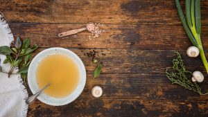 Bowl of collagen bone broth with vegetables surrounding it