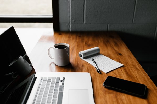 Laptop, mug, notepad with pen, and cellphone