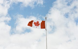 The Canadian flag flying in a cloudy blue sky