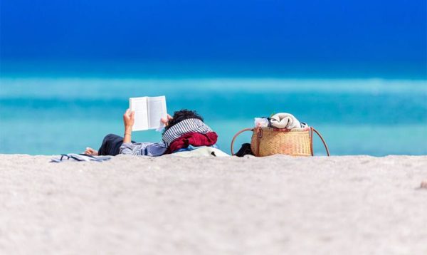 Person lying down at the beach and reading a book