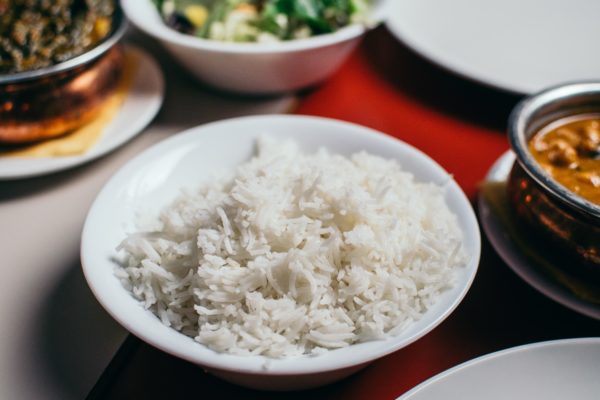 Rice in a white bowl with toppings in the background