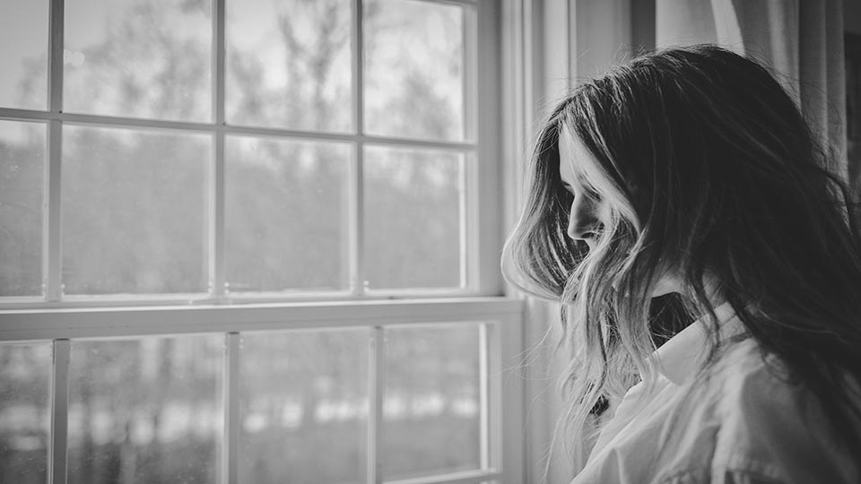 Black and white photo of woman standing by window