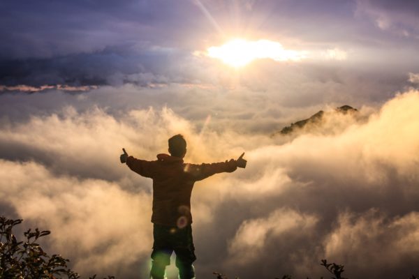 Happy man giving thumbs up against a background of clouds