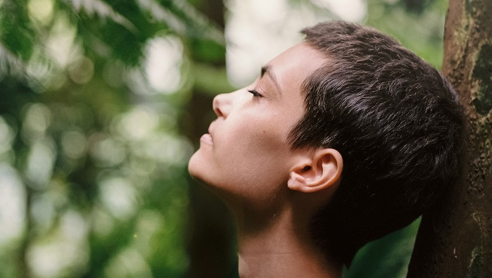 A person with short hair resting against a tree