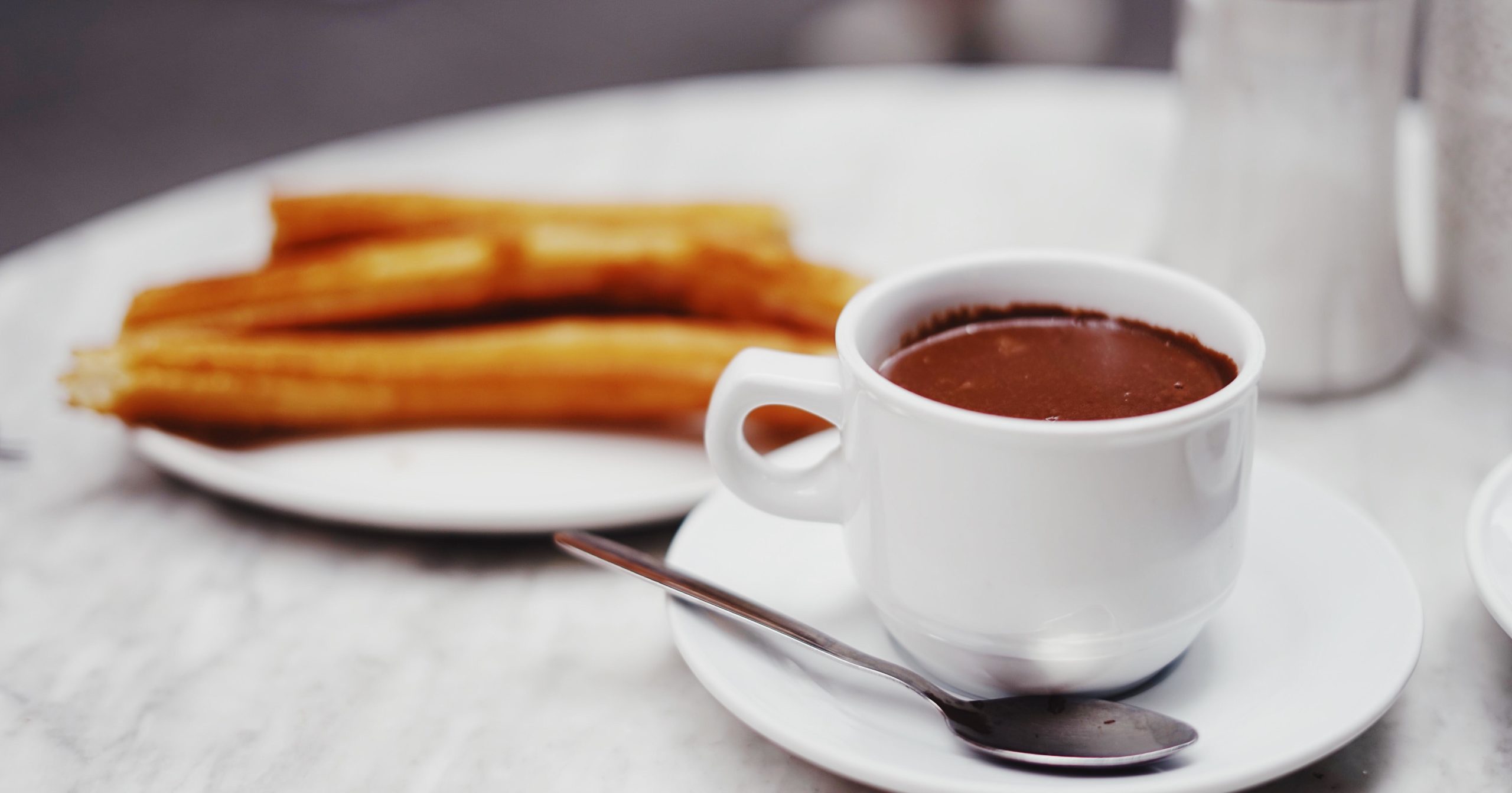 Churros on a white plate and chocolate sauce in a white mug