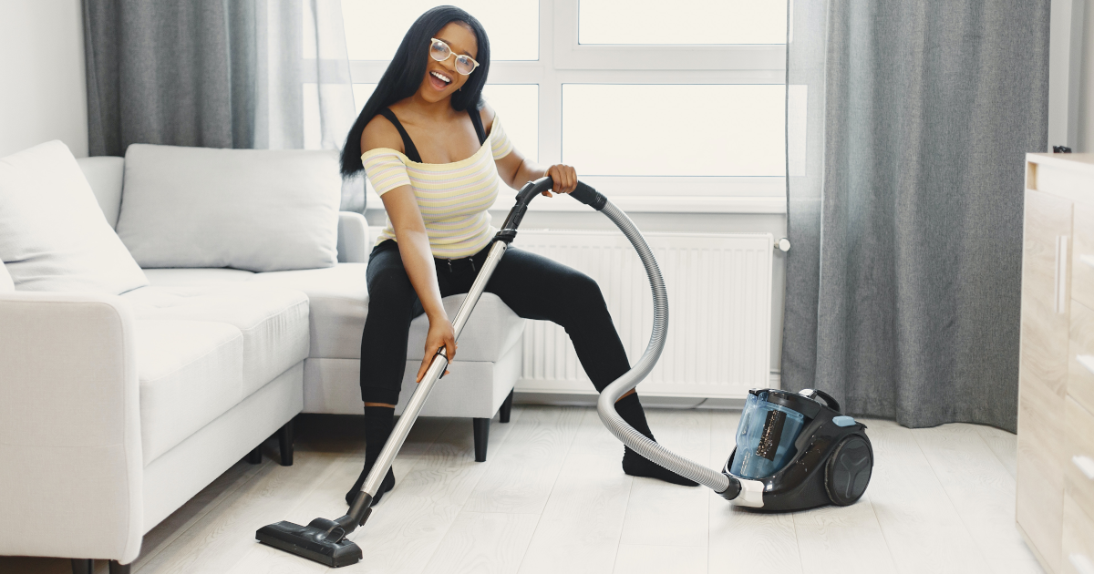 Woman vacuuming while smiling and sitting on the couch