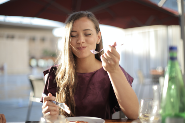 Woman eating outdoors while smiling and holding a fork