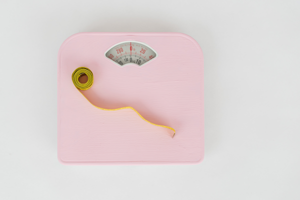 Light pink analog scale with a yellow tape measure on top